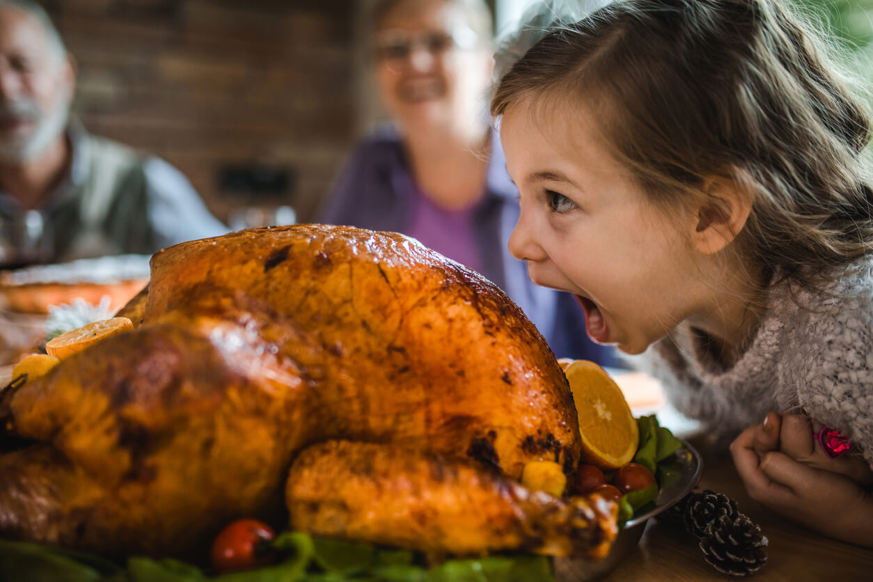 Small girl having fun while about to bite a roasted turkey on Thanksgiving.