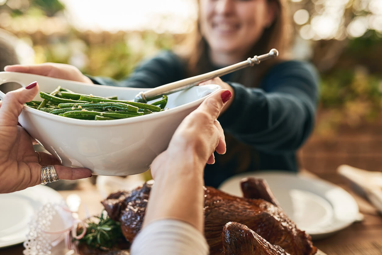 woman passing green beans at thanksgiving table