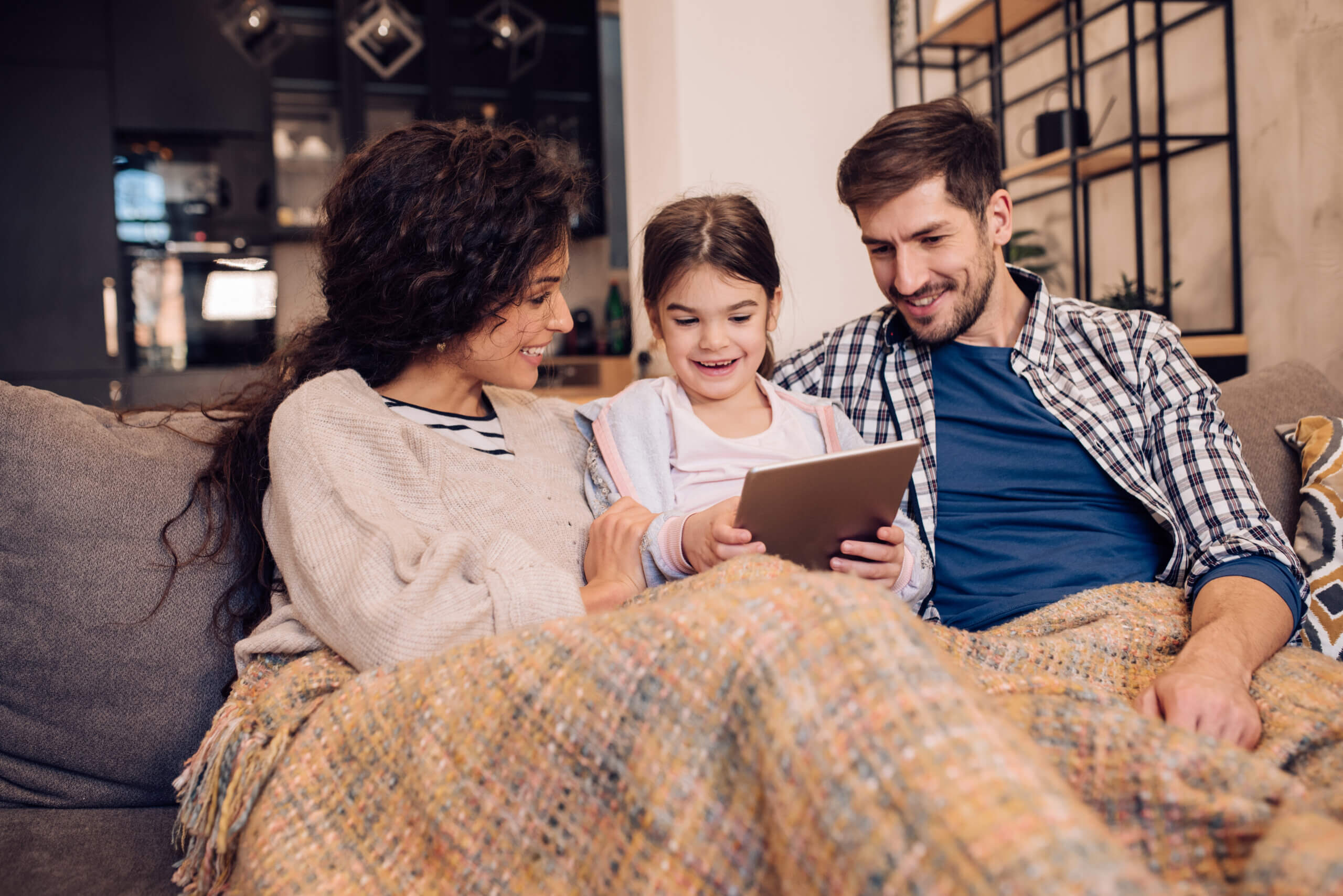 Girl enjoying on the cozy sofa with parents and using tablet