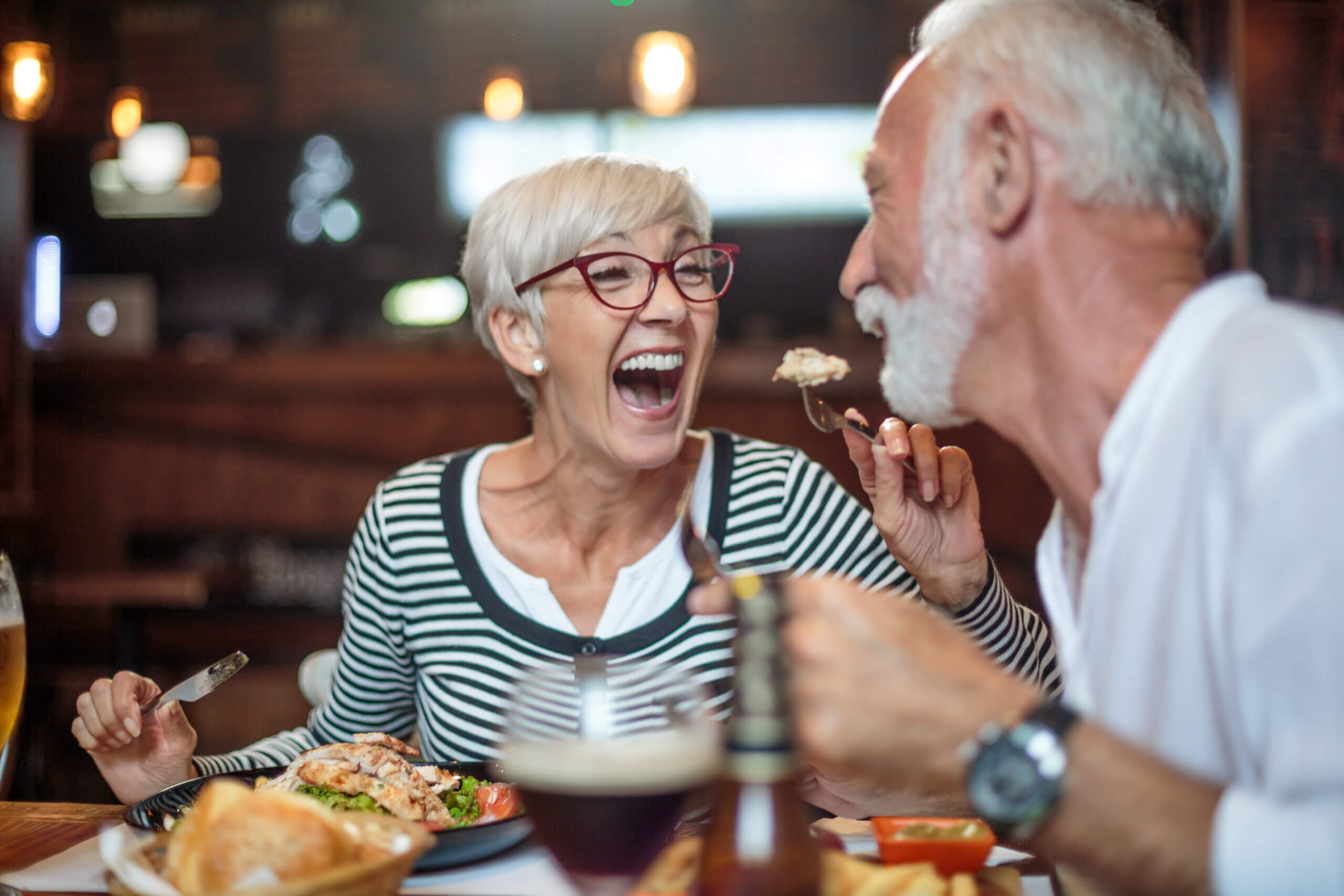 Senior woman laughing while feeding her male partner in the restaurant