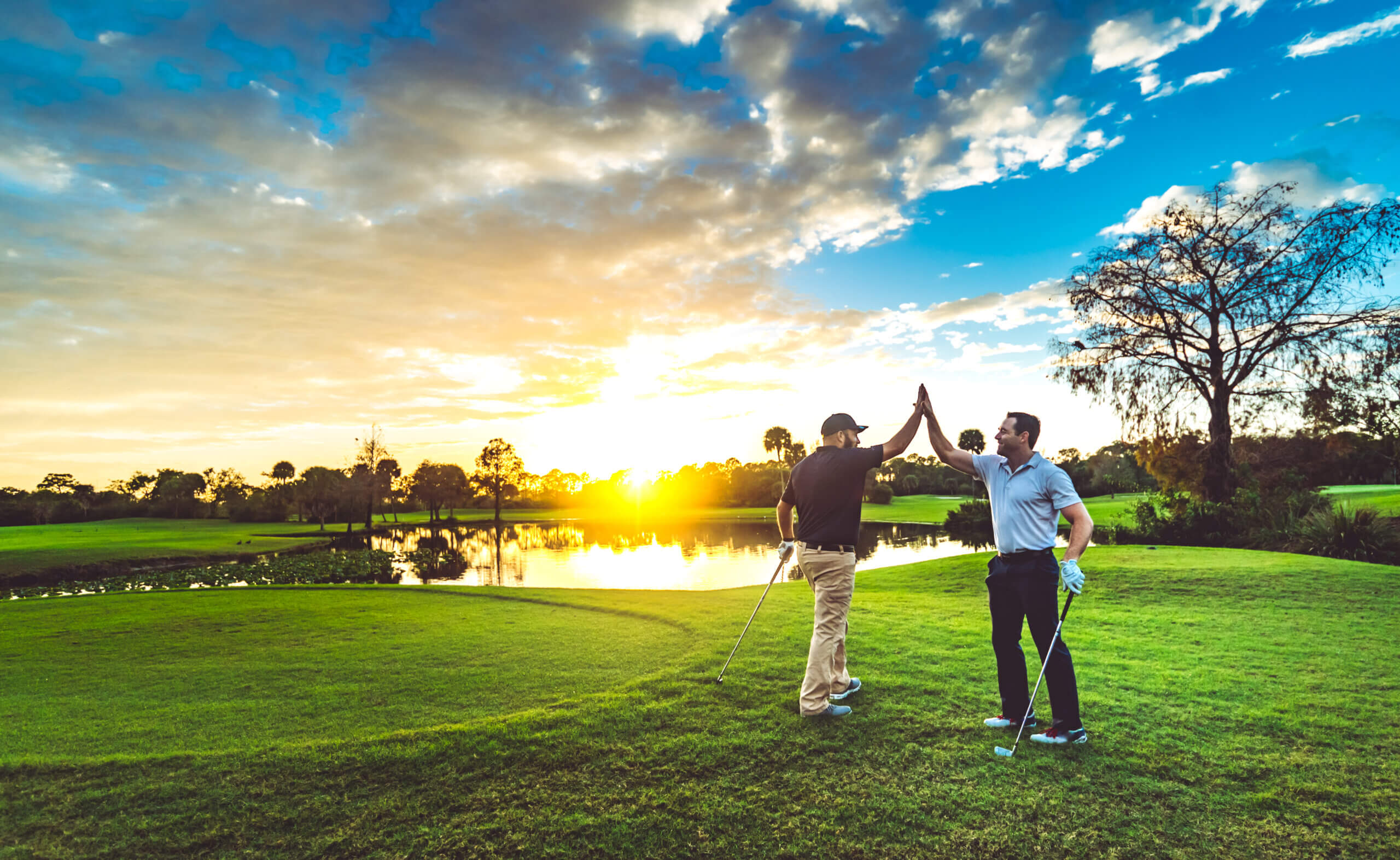 Two male golfers high five on a scenic sunset golf course