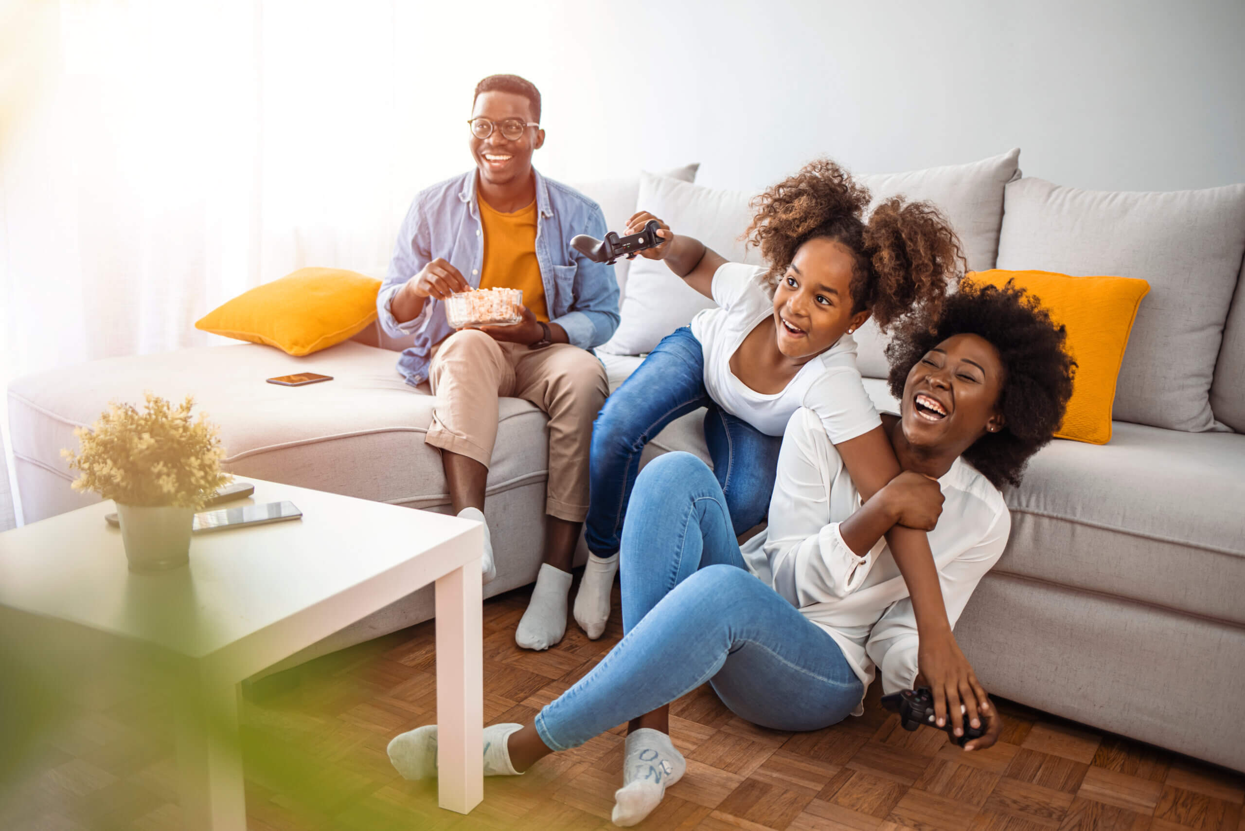 Happy family- father, mother and daughter playing a video game at home. African American family at home sitting in sofa couch and playing console video games together