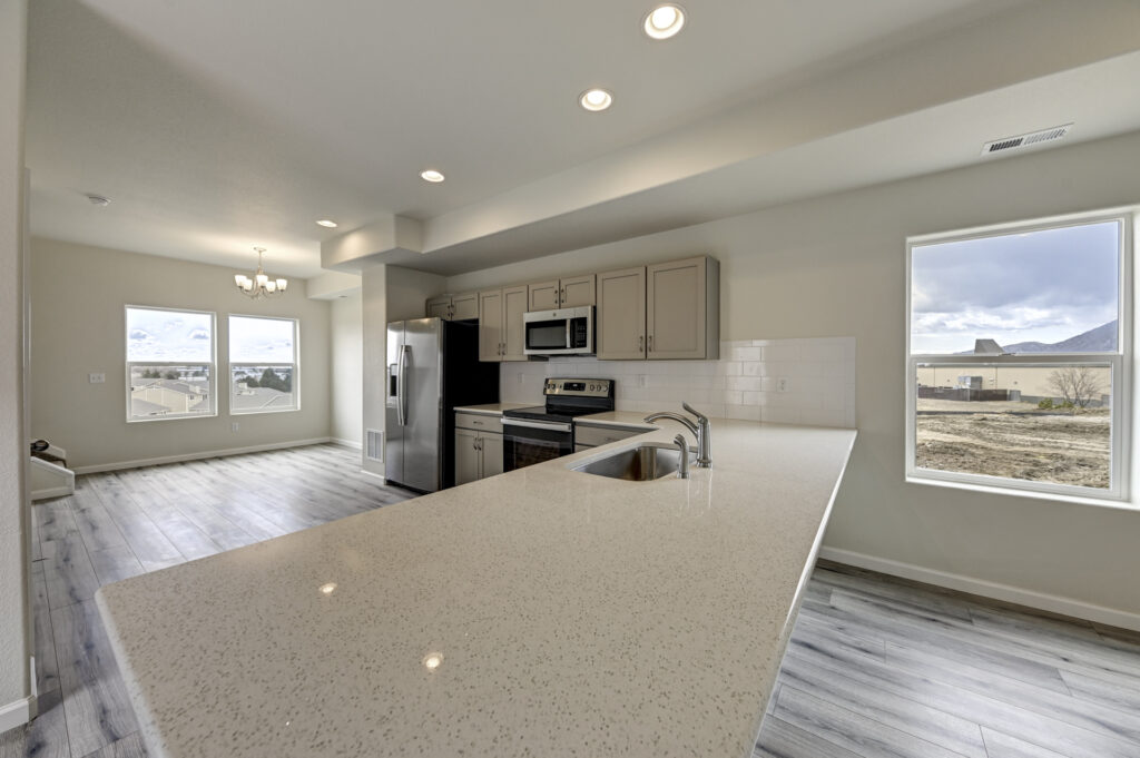 Kitchen and dining area with long quartz countertop, stainless appliances, and windows overlooking outdoors.