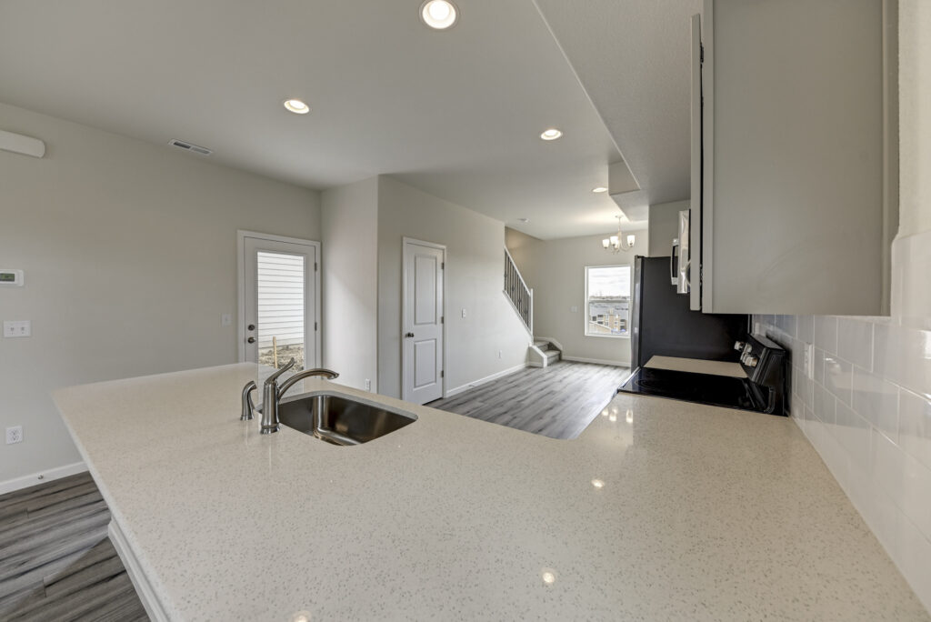 Kitchen counter foreground with sink and view toward a door, stairs, and dining area beyond.