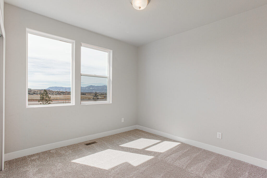 Empty carpeted room with two rectangular windows and mountain views, neutral walls and baseboards.