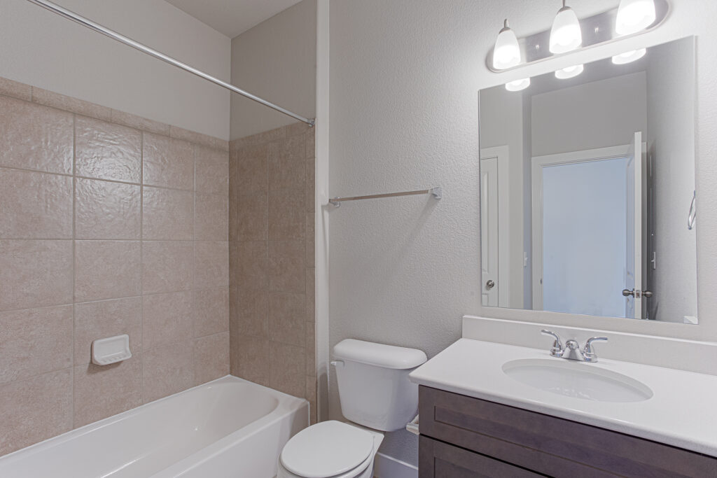 Bathroom with bathtub and tiled surround, vanity with sink and mirror, and overhead lighting.