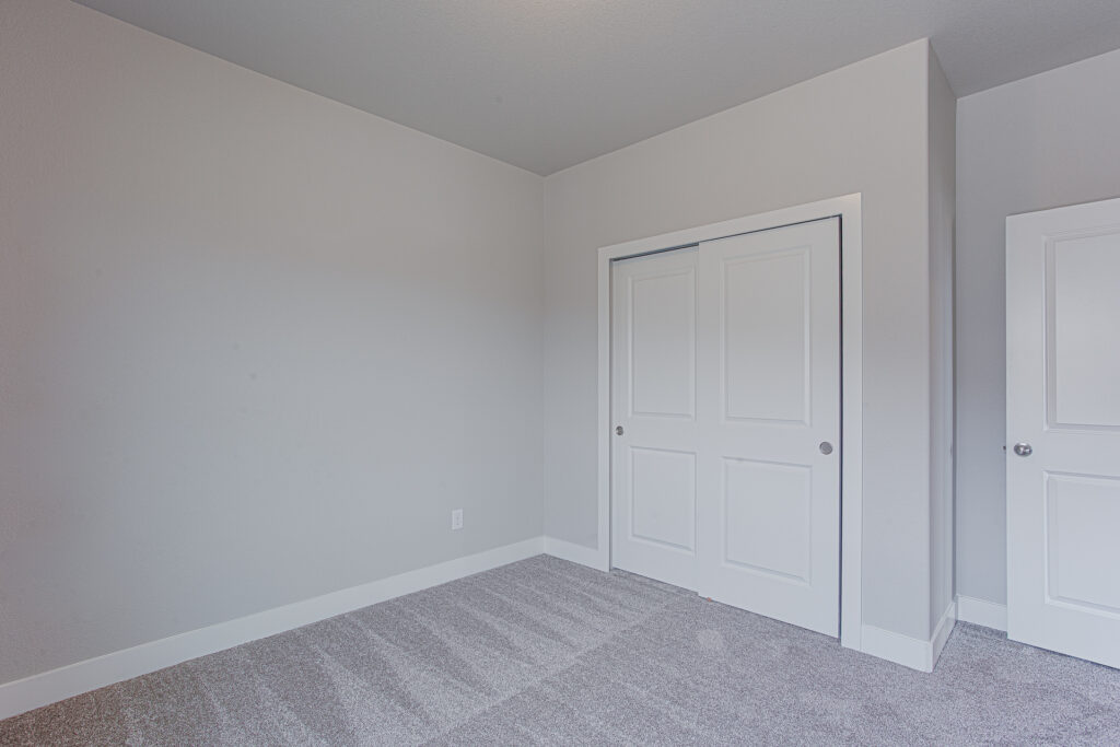 Empty carpeted room with sliding closet doors, white trim, and neutral walls.