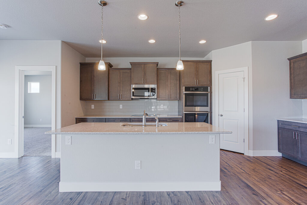 Front view of a kitchen island with sink, overhead pendant lights, and cabinetry behind.