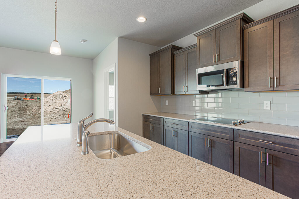 Kitchen island sink in foreground with dark cabinets and sliding patio doors in background.