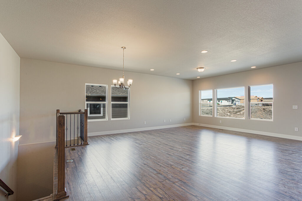 Large open living area with wood-look floors, chandelier, stair railing, and three windows.