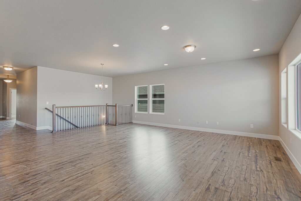 Open upstairs loft-style space with wood-look flooring, railing, and recessed ceiling lights.