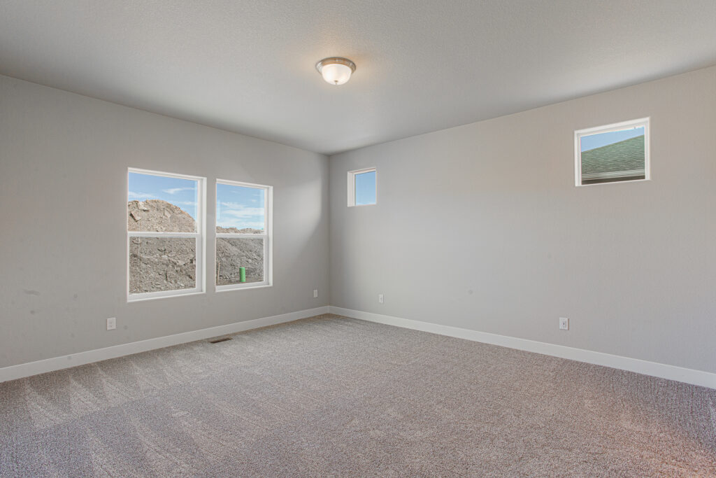 Empty carpeted bedroom or bonus room with two larger windows and two small square high windows.