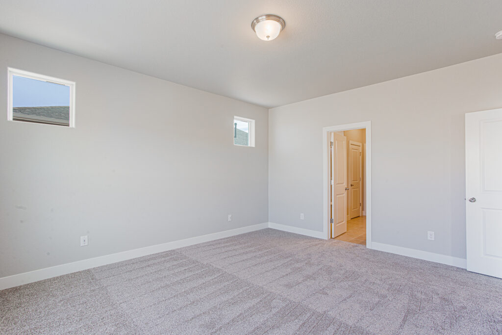 Empty carpeted bedroom with two small high windows and an open doorway to a hall.