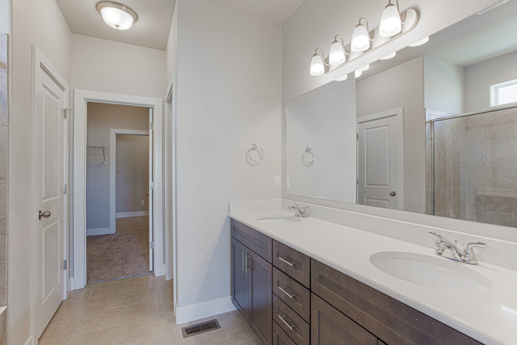 Bathroom vanity with double sinks, large mirror, and dark wood cabinets under bright lighting.
