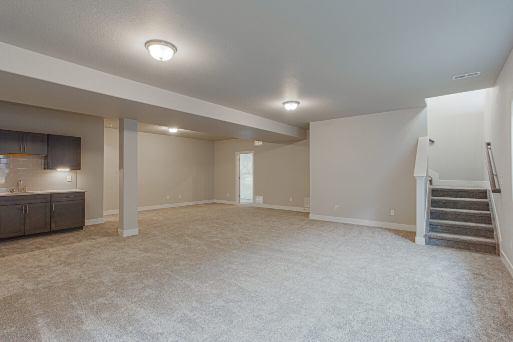Large finished basement space with carpet, support column, wet bar, and stairs.