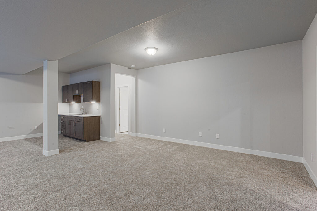 Open carpeted basement room with a wet bar or kitchenette along one wall and a support column.