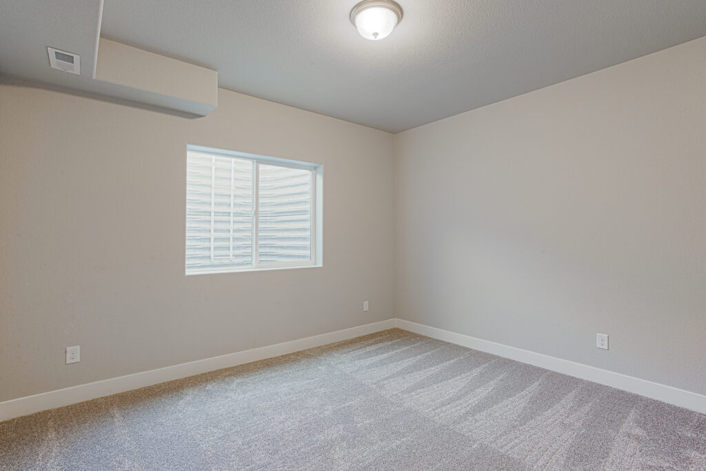 Empty carpeted bedroom or room with a window well and neutral painted walls.