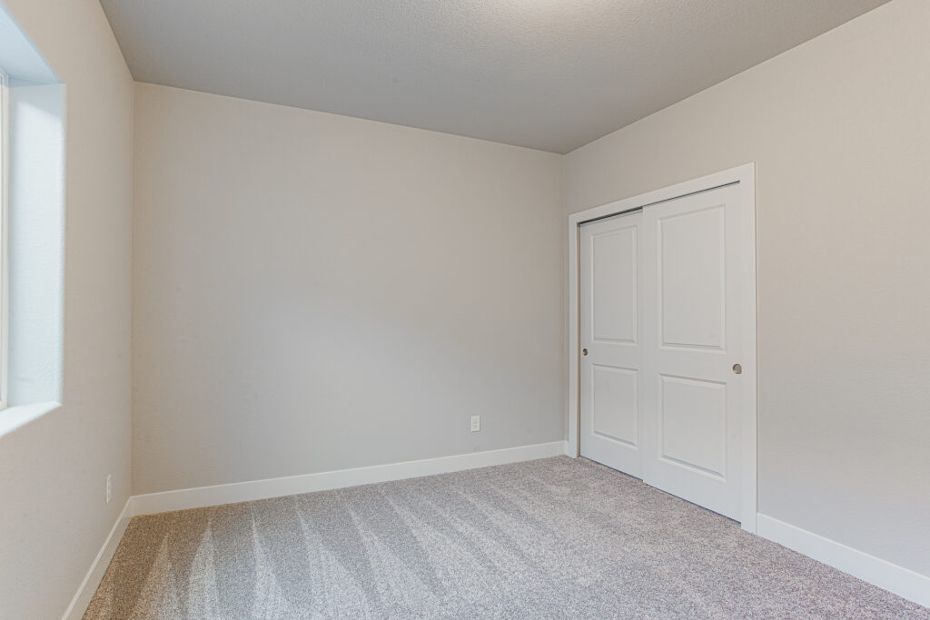 Empty carpeted room with window and sliding closet doors, neutral walls and baseboard.