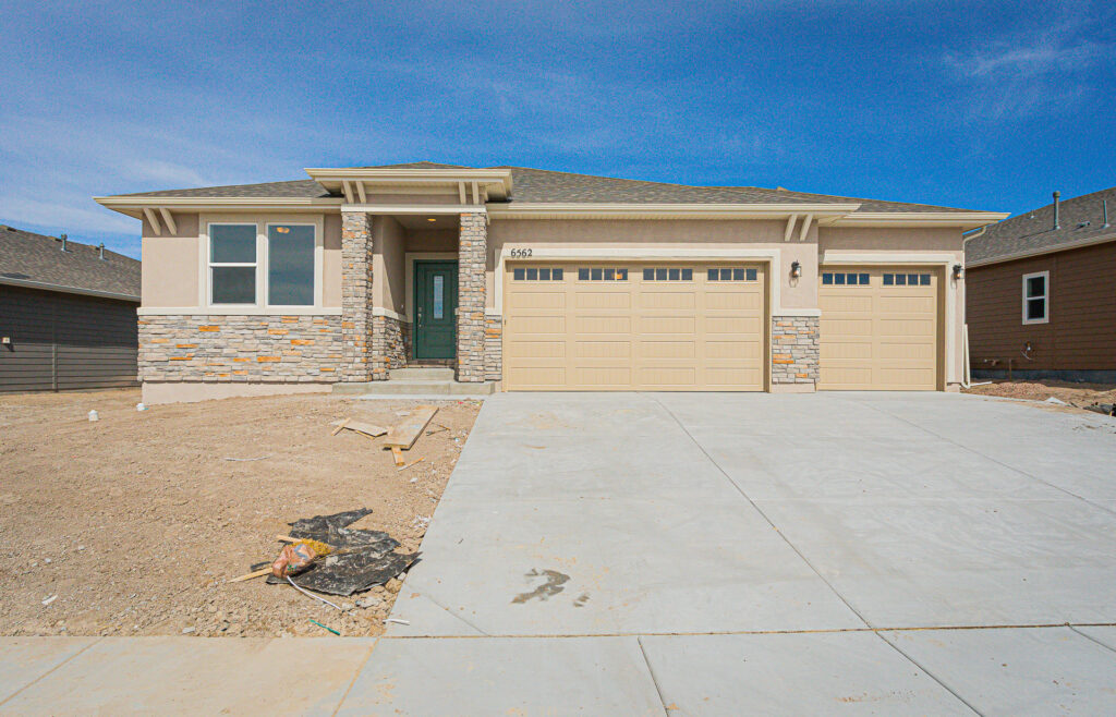 Single-story house exterior with three-car garage and stone-accented entry under blue sky.