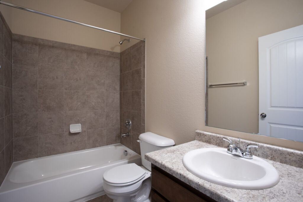 Bathroom with bathtub-shower combo, tiled surround, vanity with sink and mirror.