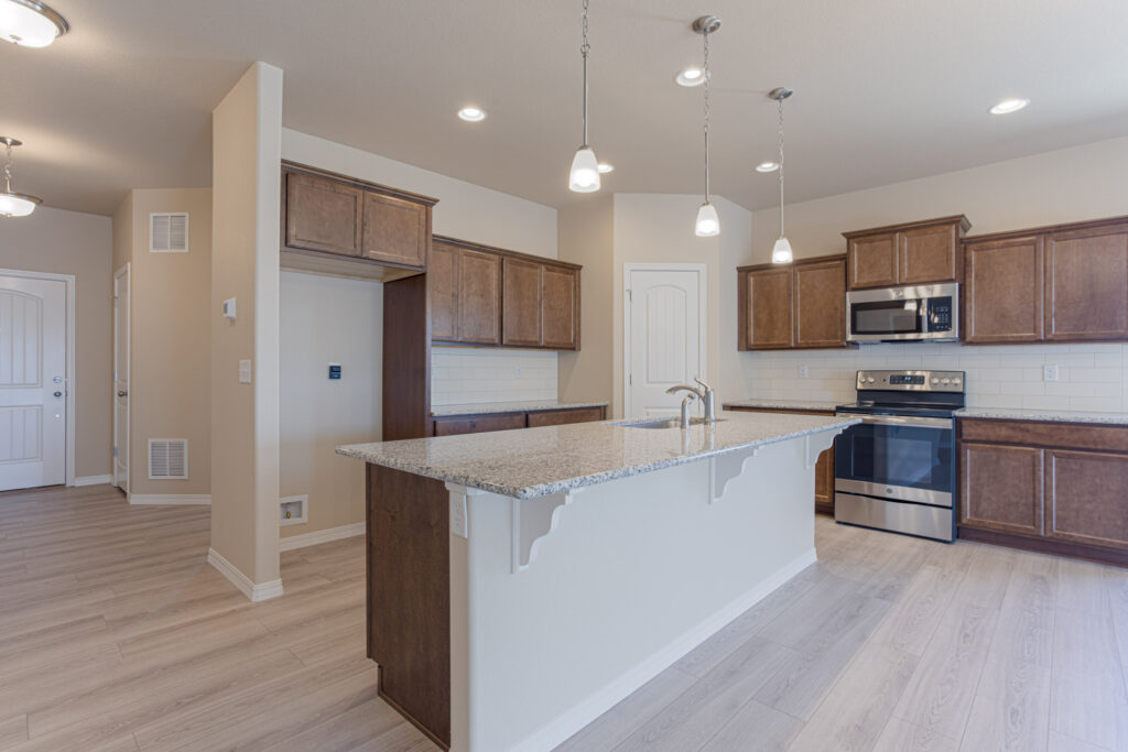 Kitchen island centered under recessed lights, stainless appliances and brown cabinets.