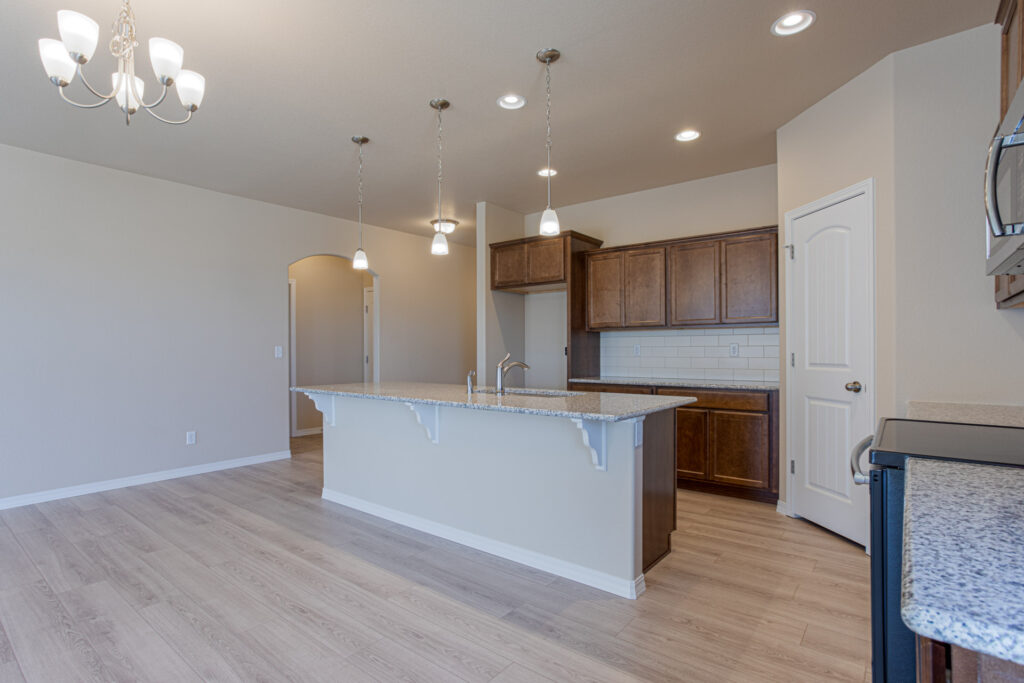 Open-plan kitchen island with pendant lights, granite counter and brown cabinets.