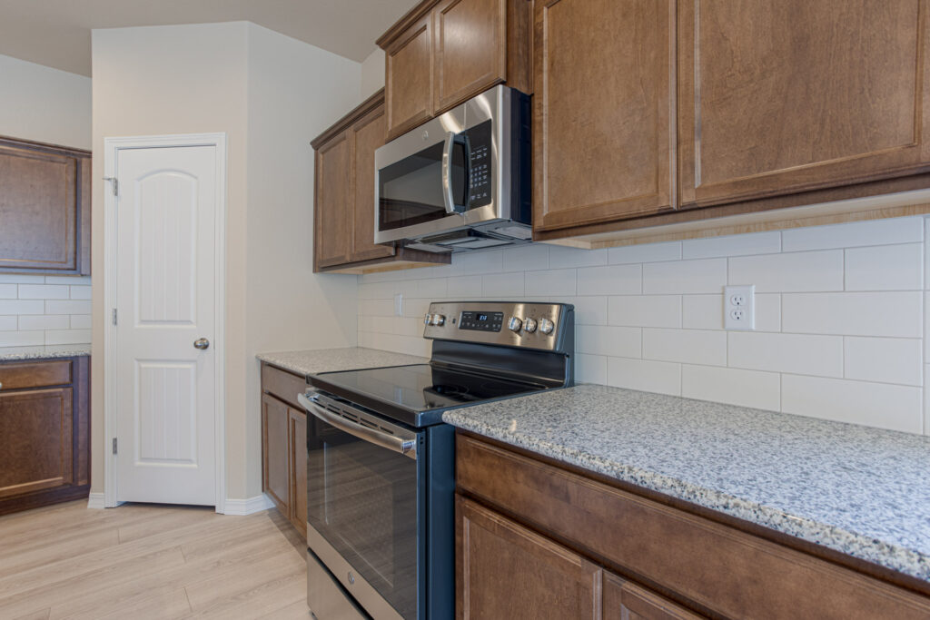 Kitchen countertop and stainless steel range with microwave, brown cabinets and white subway tile backsplash.