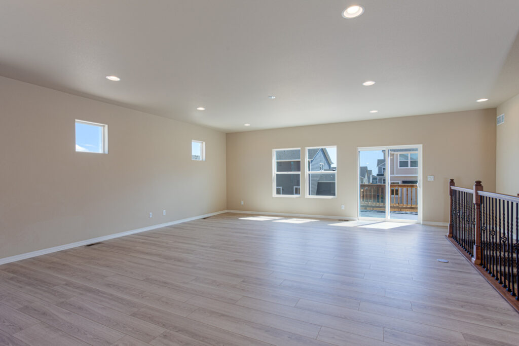 Wide open room with pale wood flooring, recessed lights, and small high windows on left wall.