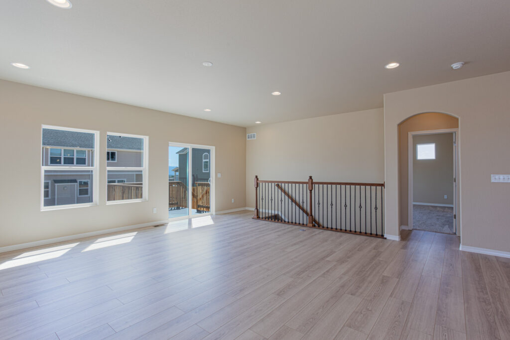 Bright living room with three windows, sliding door to deck, and railing by interior stairs.