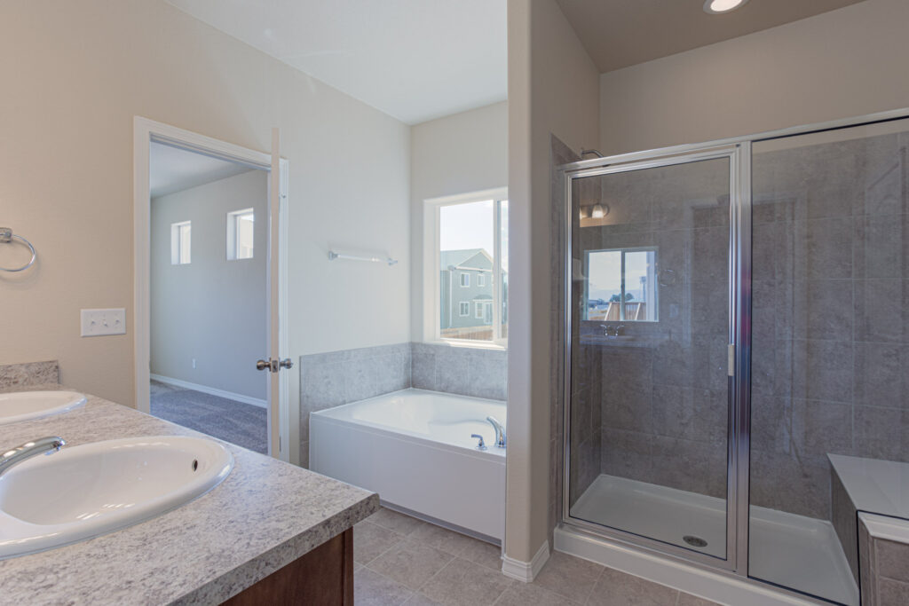 Bright bathroom with separate soaking tub, framed glass shower, and dual sinks on a stone-look counter.