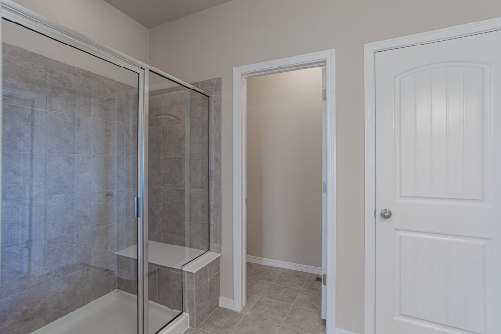Bathroom shower area with glass sliding door, tiled surround, and two interior doors nearby.