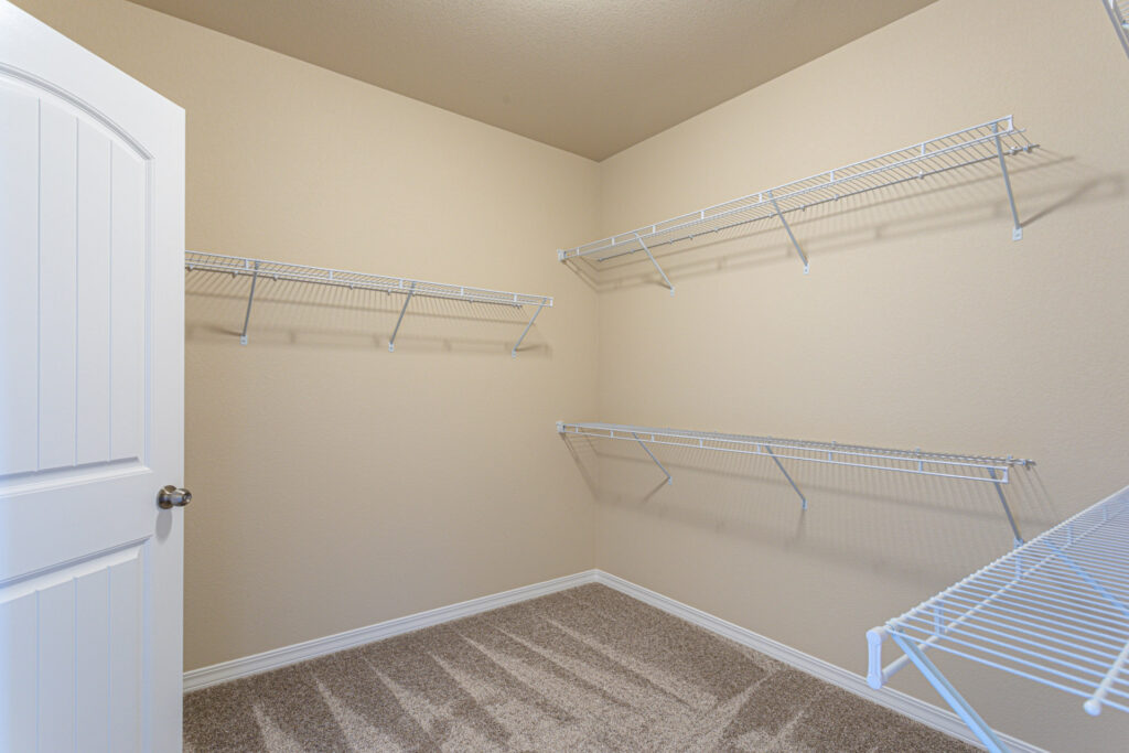 Walk-in closet with multiple white wire shelving units and beige walls.