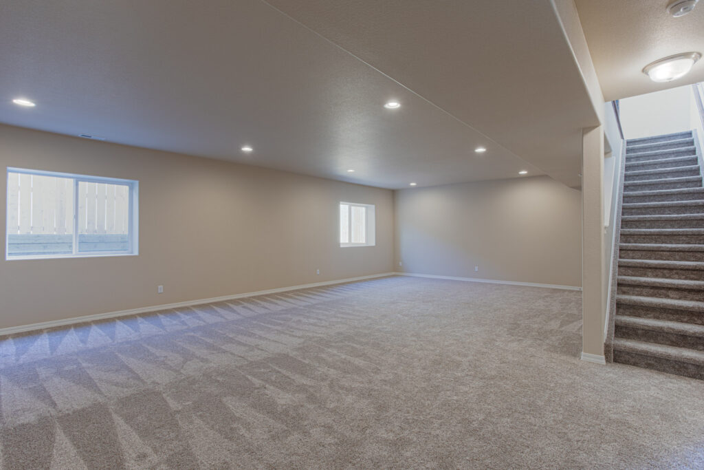 Large carpeted basement or family room with recessed lighting and two small windows.