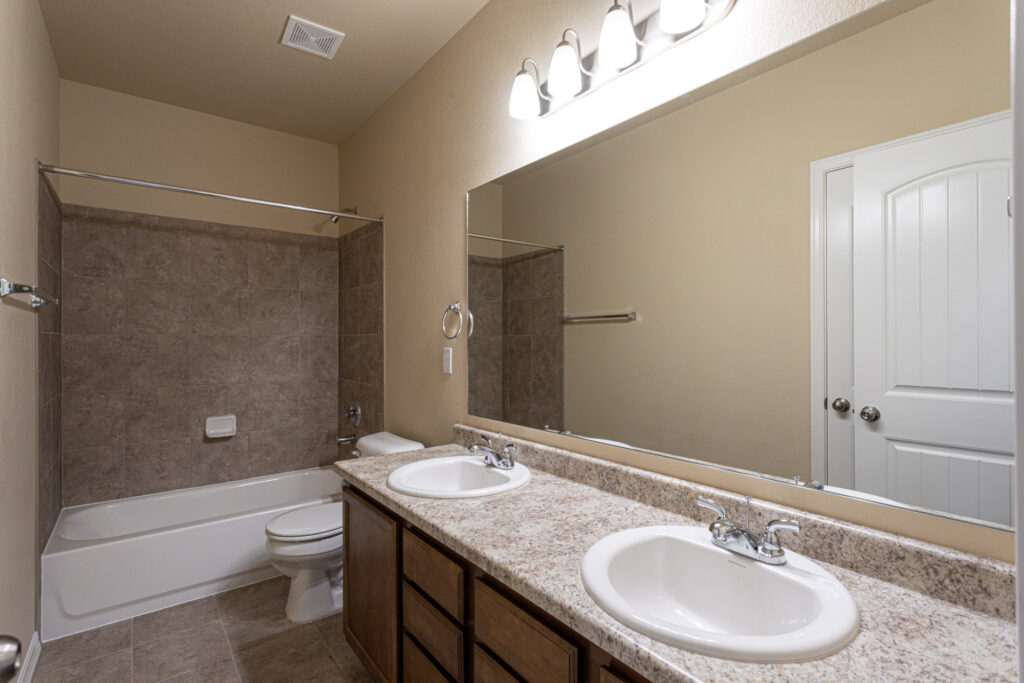 Bathroom with dual sink vanity, large mirror, and tub/shower with tiled surround.