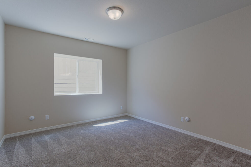 Bright empty bedroom with a single window and ceiling light fixture.