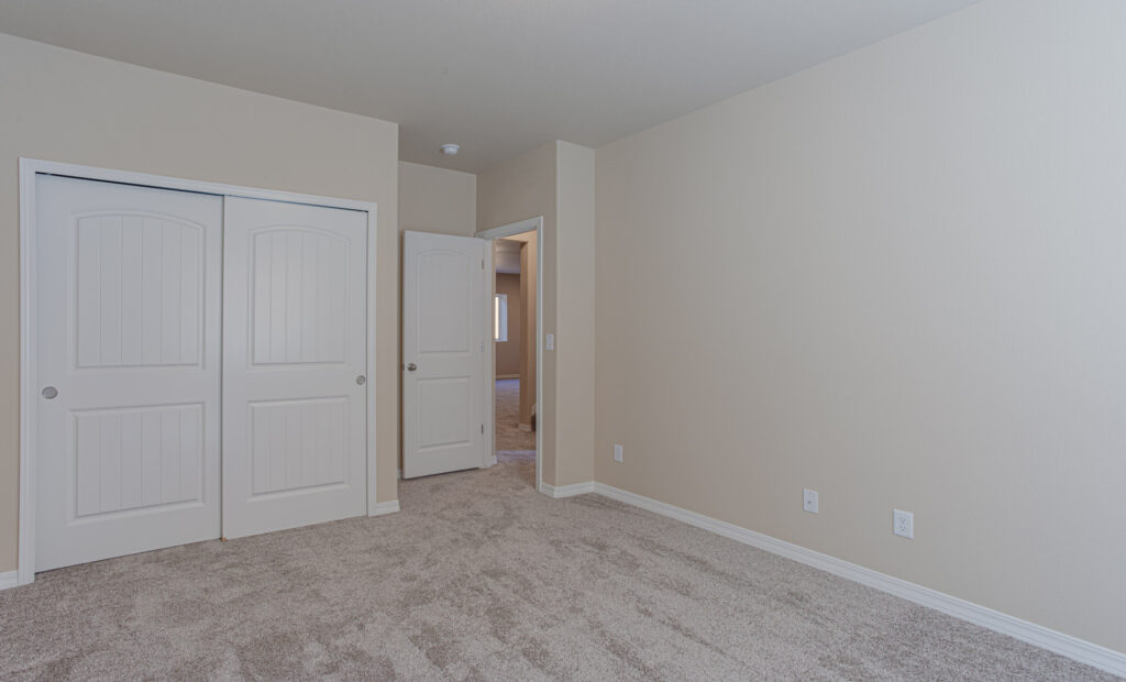 Empty carpeted room with double closet doors and an open door to a hallway.