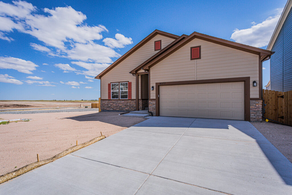 Front view of a beige house with garage and wide concrete driveway on a clear day.