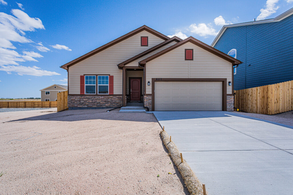 Single-story beige house with stone accents and two-car garage under a blue sky.
