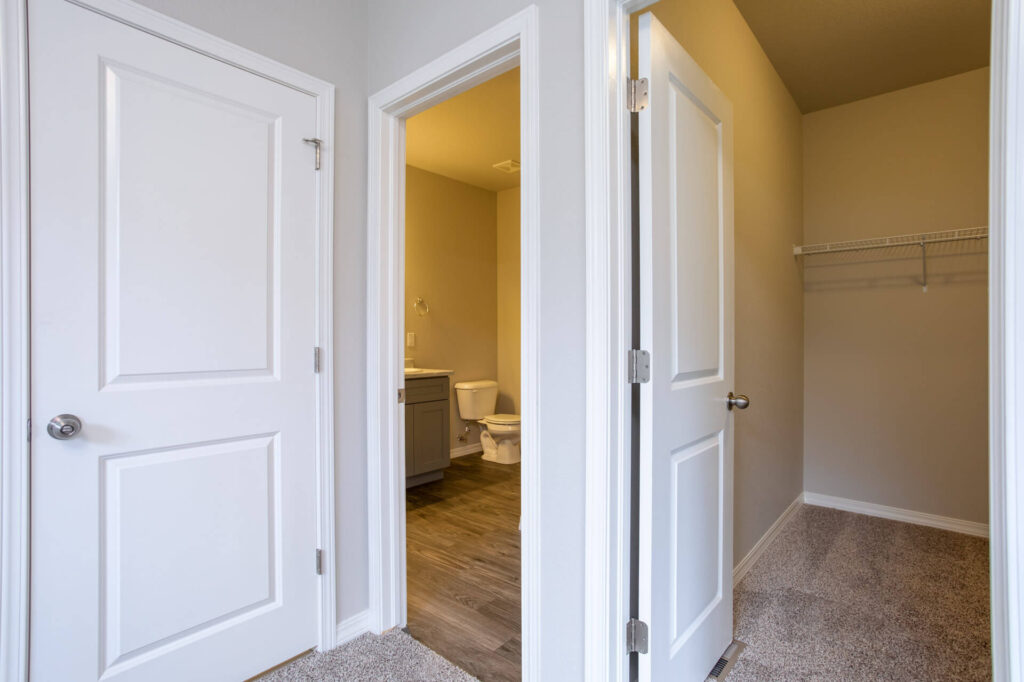 Hallway view into bathroom and carpeted closet with three white interior doors.