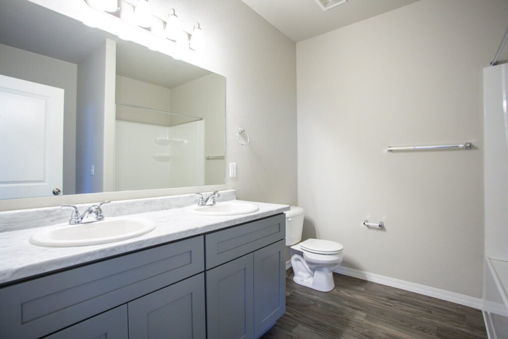 Bright bathroom with double sink vanity, large mirror, toilet, and shower-tub combo.