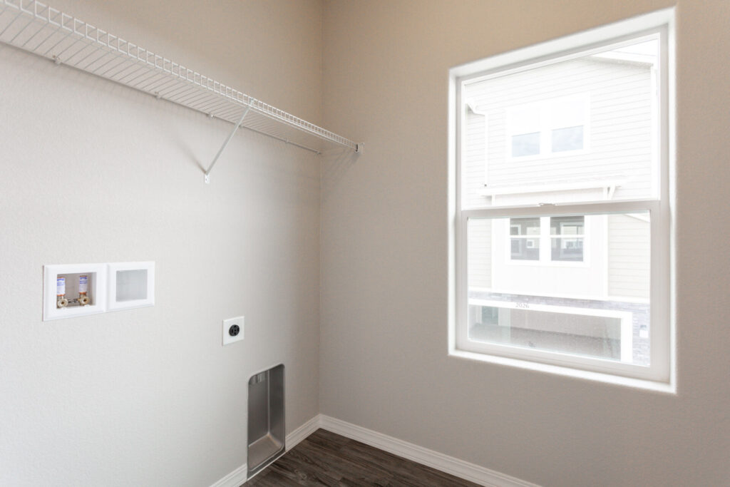 Laundry room with wire shelf, washer/dryer hookups, and a window looking outside.