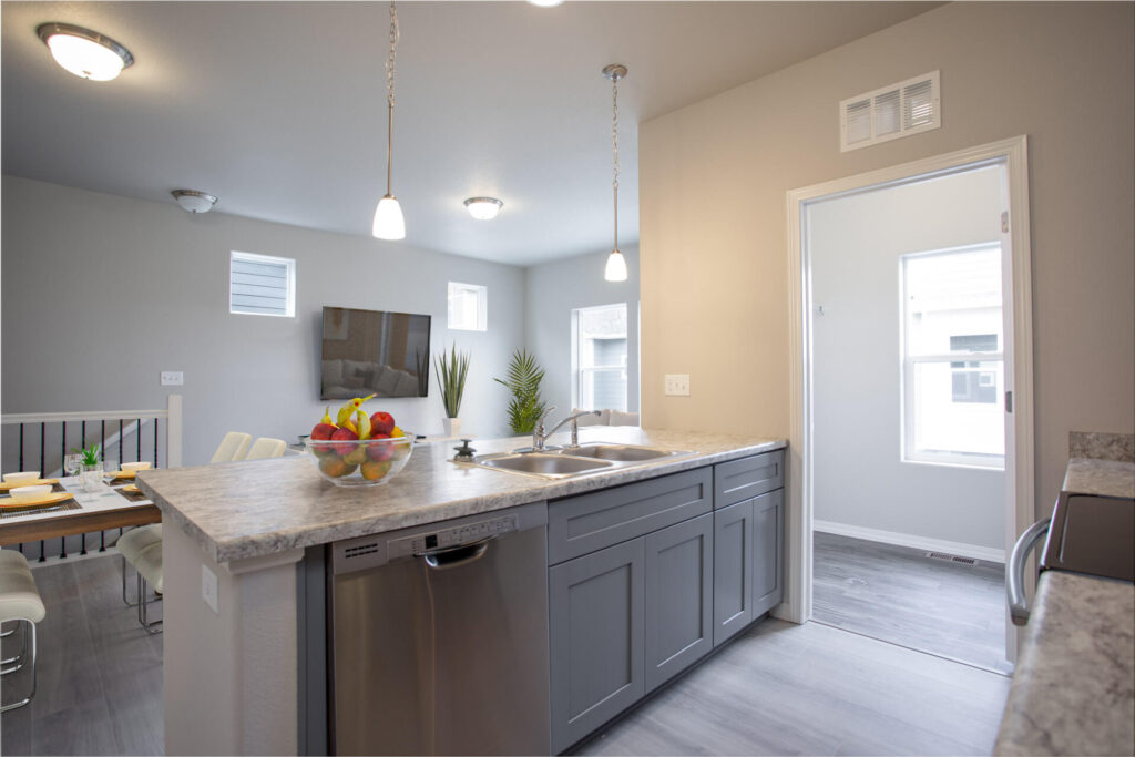Kitchen island with sink, dishwasher, pendant lights, and open view into a dining area and living room.
