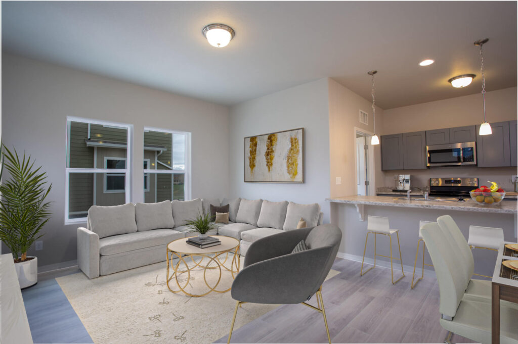 Open-plan living room and kitchen with sectional sofa, bar stools at the island, and pendant lights.