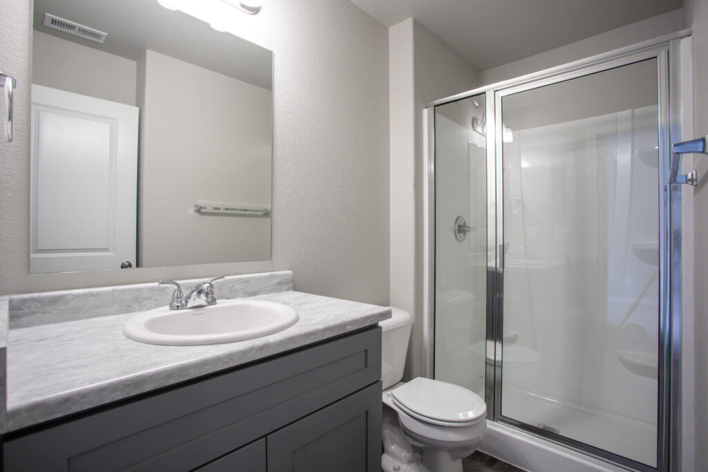 Bathroom with single-sink vanity, mirror, toilet, and corner glass shower enclosure.