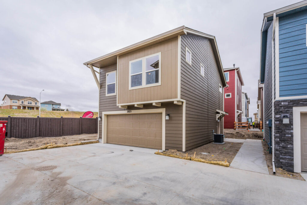 Two-story brown exterior house with attached double garage and concrete driveway in a new development.