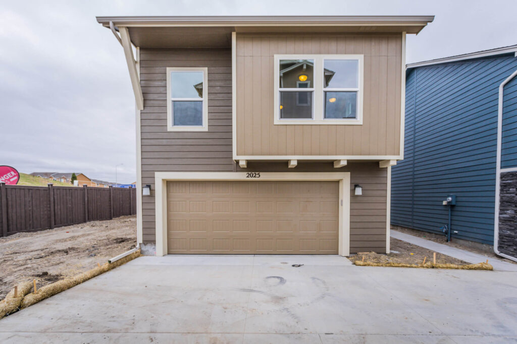 Two-story detached house with upper-level windows and double garage facing a concrete driveway.