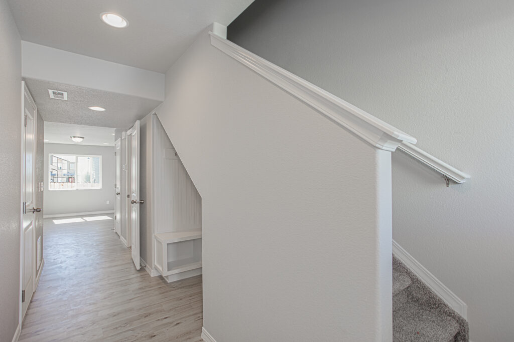 Hallway beside a staircase with white handrail, light flooring, and a small built-in bench under the stairs.