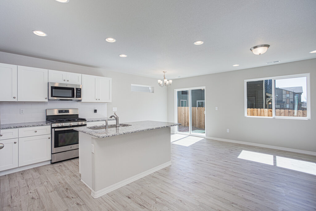 Open bright kitchen and dining area with island, stainless appliances, and sliding glass door.