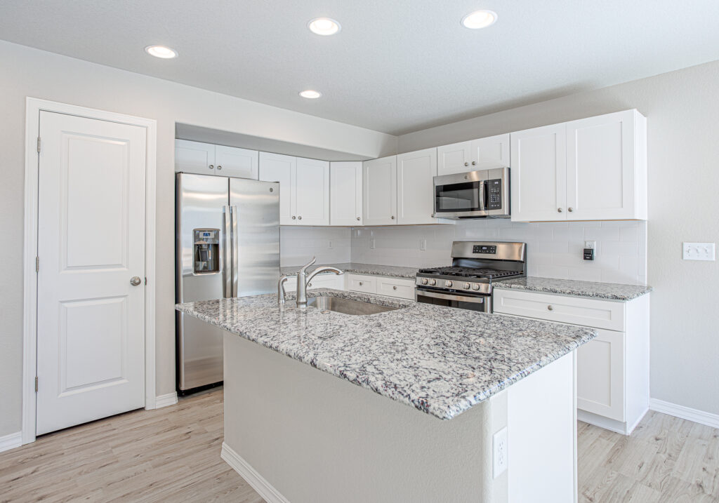 Kitchen island with granite countertop, stainless refrigerator, white cabinets and recessed lighting.