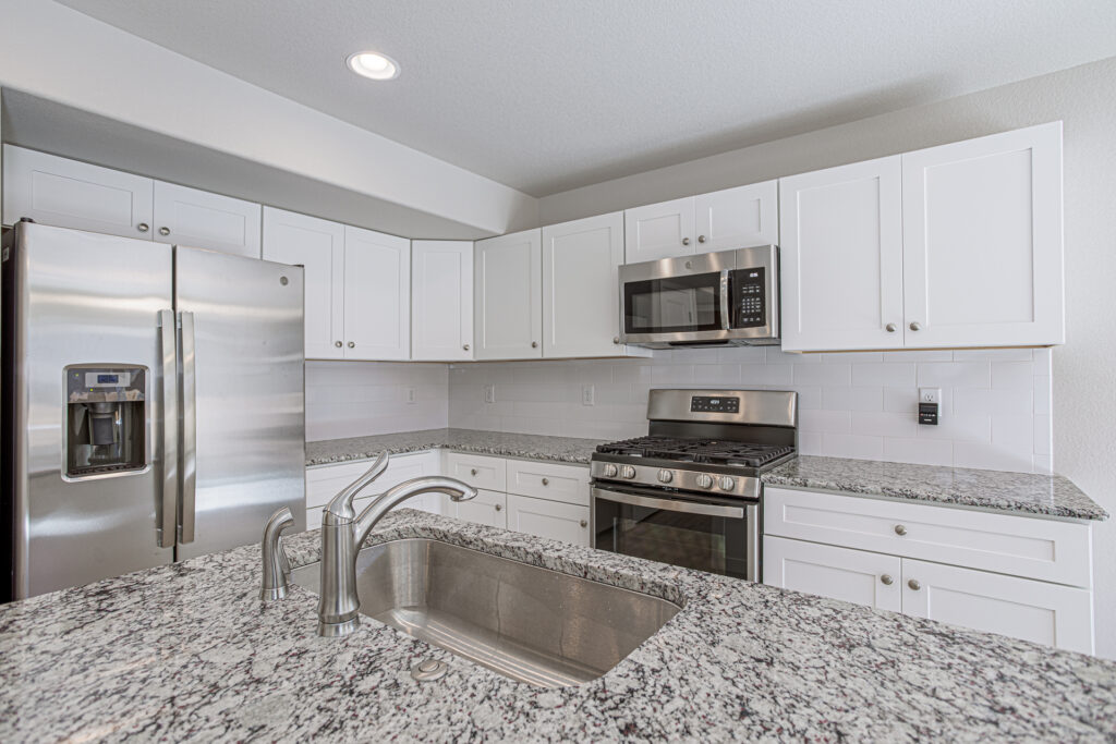 Close-up of kitchen island sink with granite counters, stainless refrigerator, stove and microwave.